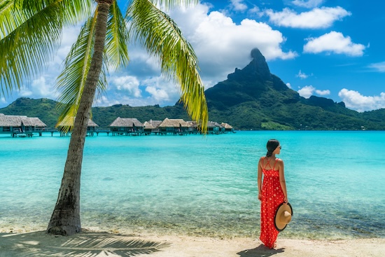 Bora Bora luxury hotel vacation tourist woman relaxing by ocean beach with view of Mt Otemanu in Tahiti, Frenc Polynesia. High End resort with overwater bungalows villas @ credit Depositphotos