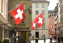 Suisse | La Suisse championne de l’inhospitalité ? Encore un « drôle » de sondage ! Zurich, Switzerland - June 03, 2017: People on the street of Zurich decorated with flags of Switzerland. Swiss Flags on the facade building in historic city center of Zurich, Switzerland @ credit Depositphotos