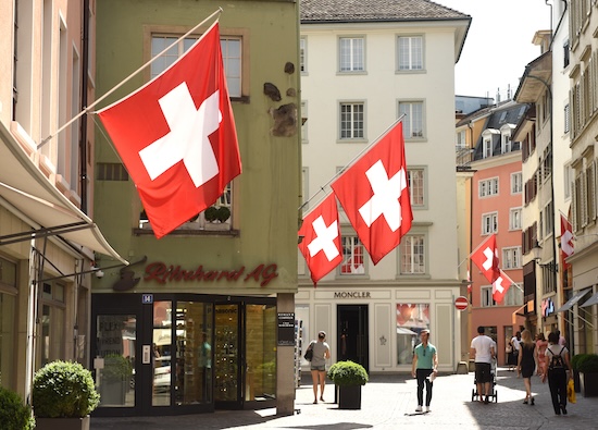 Zurich, Switzerland - June 03, 2017: People on the street of Zurich decorated with flags of Switzerland. Swiss Flags on the facade building in historic city center of Zurich, Switzerland @ credit Depositphotos