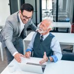 Senior boss happy for good online work result of young male businessman.