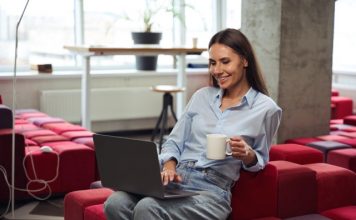 Point de droit | Télétravail : la Cour de cassation confirme le droit aux titres-restaurant pour tous les salariés Cheerful young woman with teacup in hand looking at computer monitor while sitting on chair in comfortable coworking space